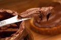 Knife full of sweet chocolate nougat spread on glass jar.