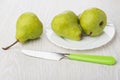 Knife, green pears in glass plate and on wooden table