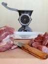 Knife and meat for mince on a wooden cutting board. Behind them are a vintage manual meat grinder and a white plate on a beige bac Royalty Free Stock Photo