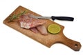 Knife on raw red mullet fillets laid on a cutting board with a slice of lemon and rosemary close-up on white background