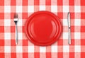 Knife, red plate and fork on checked tablecloth Royalty Free Stock Photo