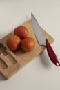Knife with red tomatoes ready to chop and prepare homemade food with wooden board on white table