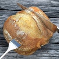 A knife is slicing a bread campaign on a wooden and old table.