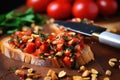 a knife spreading tomato topping on a bruschetta, pine nuts loosely scattered