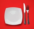 Knife, square white plate and fork on red top view