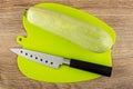 Knife, squash marrow on green cutting board on wooden table. Top view