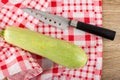 Knife, squash marrow on napkin on wooden table. Top view