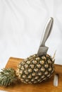 A knife stuck in a pineapple on a board on a white background Royalty Free Stock Photo