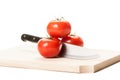 Knife between three tomatoes on wooden board Royalty Free Stock Photo