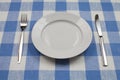 Knife, white plate and fork on blue tablecloth