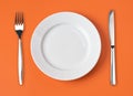 Knife, white plate and fork on orange top view