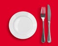 Knife, white plate and fork on red top view