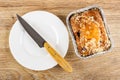 Knife on white plate, muffin with raisin in foil mold on wooden table. Top view