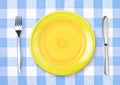 Knife, yellow plate and fork on checked tablecloth