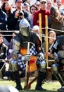 A knight in a metal helmet and bright armour with a sword in his hand, an element of a costume performance at a medieval fair