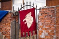 Knight`s Tournament. A knight`s red flag with a white wolf on the iron bars of the gate Royalty Free Stock Photo