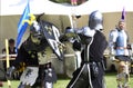 Knights in metal helmets and armour with swards fight, a part of a costume performance at a medieval fair