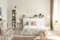 Knit blanket in basket standing on dirty pink carpet in real photo of bright feminine bedroom interior with