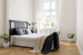 Knit blanket on bed in minimal white bedroom interior with plant