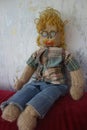 Knitted and crocheted male doll in the shape of a blond man with a mustache, curly hair, glasses, jeans and checked shirt.
