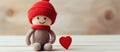 A knitted doll in a red hat and scarf sitting next to a red heart Royalty Free Stock Photo