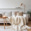 Knitted fringed blanket on white sofa, wooden coffee table with candles on carpet near it. Scandinavian, hygge interior design