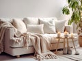 Knitted fringed blanket on white sofa, wooden coffee table with candles on carpet near it. Scandinavian, hygge interior design of