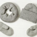 Knitted grey mittens, hat and scarf on white wood background. Fashionable warm clothes Royalty Free Stock Photo