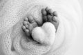 Knitted heart in the legs of baby. The tiny foot of a newborn baby.