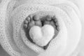 Knitted heart in the legs of baby. The tiny foot of a newborn baby.