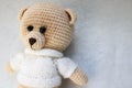 A knitted homemade beautiful cute little bear in a white sweater with black eyes, a soft toy tied with beige large threads on a li Royalty Free Stock Photo