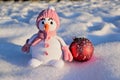 A knitted snowman girl stands in the snow next to a large Christmas tree toy