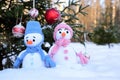 Knitted snowmen in colorful clothes stand in the snow under a Christmas tree decorated with toys Royalty Free Stock Photo