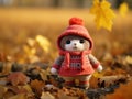 a knitted teddy bear in a red coat standing in a pile of fallen leaves