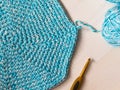 Knitted Turquoise circle carpet and crochet and yarn ball on wooden table.