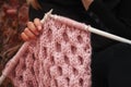 Knitting on knitting. Hands close-up knitting on knitting needles, pink wool knit against the backdrop of a natural garden. Needle