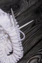 Knitting with needles. A skein of white thread and a fragment of a knitted product. On black pine boards. Close-up