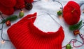 Knitting a red Christmas sweater on the background of New Year`s decor with a garland.