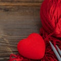 Knitting sticks and red yarn and little red heart on old wooden background. Square