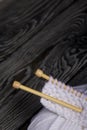 Knitting with wooden needles. A skein of white thread and a fragment of a knitted product. On black pine boards. Close-up