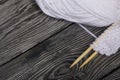 Knitting with wooden needles. A skein of white thread and a fragment of a knitted product. On black pine boards. Close-up