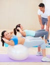 She knows her workouts will pay off. Young woman doing a sit up during a pilates class with the help of an instructor.