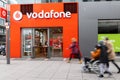 Facade and shop window of the Vodafone store with passengers in motion blur in front.