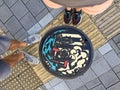 Top view of male and female legs standing in front of a Japanese manhole