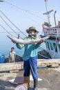 Thai fisherman shows caught fish on the pier near fishing boat on the island Koh Phangan, Thailand Royalty Free Stock Photo