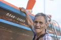 Thai old fisherman is standing near his wooden boat near the shore on the island Koh Phangan, Thailand Royalty Free Stock Photo