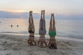 Three young girl practice yoga headstand asana on sea shore at sunset on the tropical island of Koh Phangan, Thailand