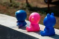 Group of three cute small toys sitting on wall under bright sunlight on blur