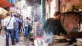 An Indian man making tea at his chai stall on a crowded market street in the city of