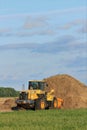 A Komatsu front end loader by a dirt pile ready for work with green grass and blue sky out in the country.